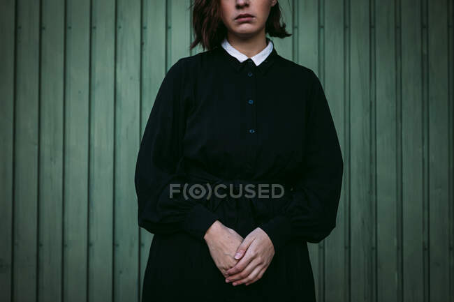 Cropped unrecognizable female in black dress standing against wooden wall of house — Stock Photo