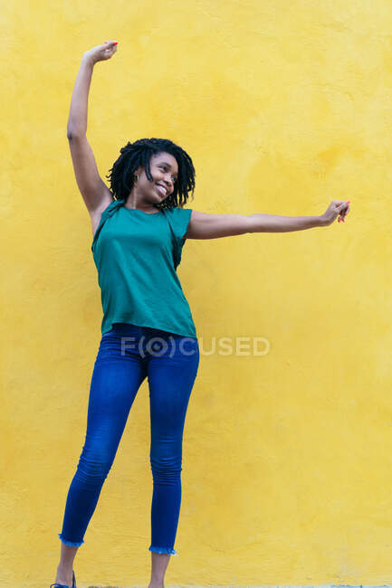 Riendo joven mujer africana delante de la pared amarilla con los brazos levantados - foto de stock