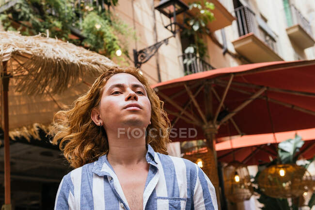 Peaceful male with long hair standing in street and enjoying freedom while looking away — Stock Photo