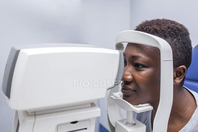 Mulher negra em gabinete de optometria durante o estudo da visão usando um retinógrafo moderno — Fotografia de Stock