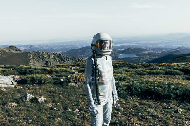 Astronauta masculino em trajes espaciais e capacete em pé na grama e pedras em terras altas — Fotografia de Stock