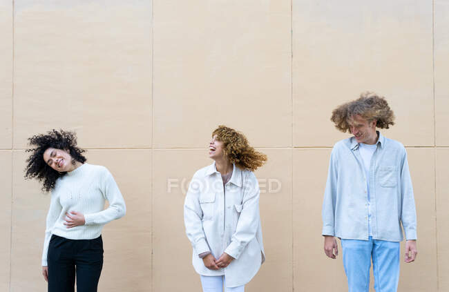 Groupe de jeunes femmes diverses et l'homme avec les cheveux bouclés debout en rangée contre le mur beige avoir du plaisir — Photo de stock