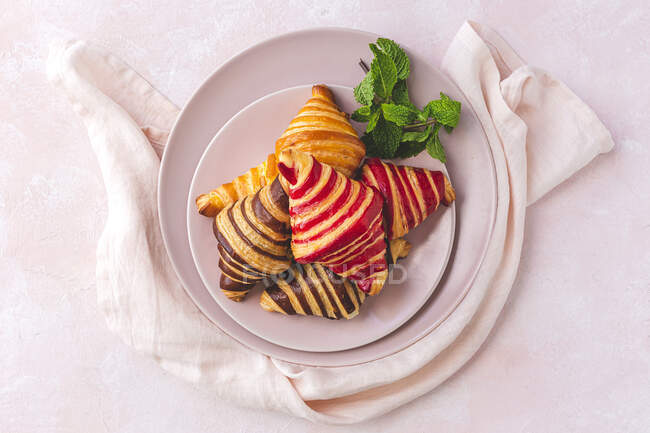 Vista superior de deliciosos croissants colocados en el plato con ramita de menta sobre fondo rosa pastel - foto de stock