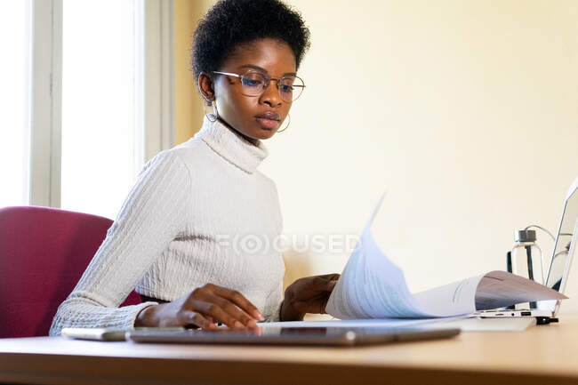 Лікар - афроамериканка сидить за столом з ноутбуком і читає медичні записи під час роботи в клініці. — стокове фото