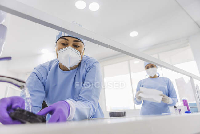 Desde abajo el dentista del cultivo lava chapas con agua limpia en fregadero en clínica dental - foto de stock