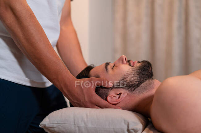 Вид сбоку на анонимного массажиста, делающего тайский массаж для мужчин в современном спа-салоне — стоковое фото