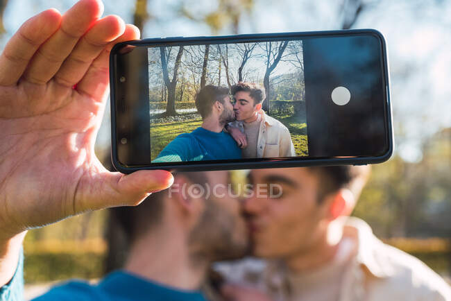 Fröhliches Paar homosexueller Männer umarmt sich und schießt sich im Park auf Handy — Stockfoto
