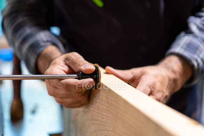 Crop anonymous male carpenter working with professional wheel marking gauge and wooden plank in workshop — Stock Photo