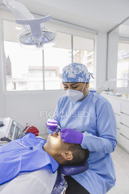 Médica em dentes de limpeza uniformes de paciente do sexo masculino com afastador dentário no hospital — Fotografia de Stock