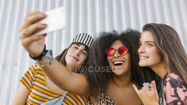 Три красивые молодые женщины разных рас с длинными досками для смартфона делают селфи. — стоковое фото