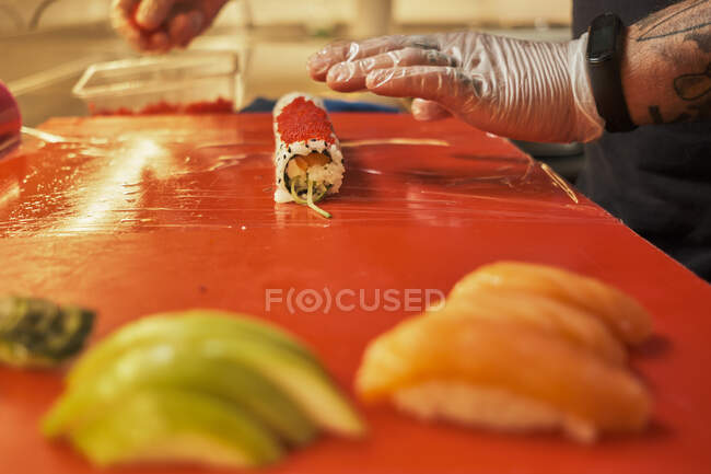 Cultivo irreconhecível cozinheiro masculino preparando rolos apetitosos com arroz e salmão na cozinha do restaurante japonês — Fotografia de Stock