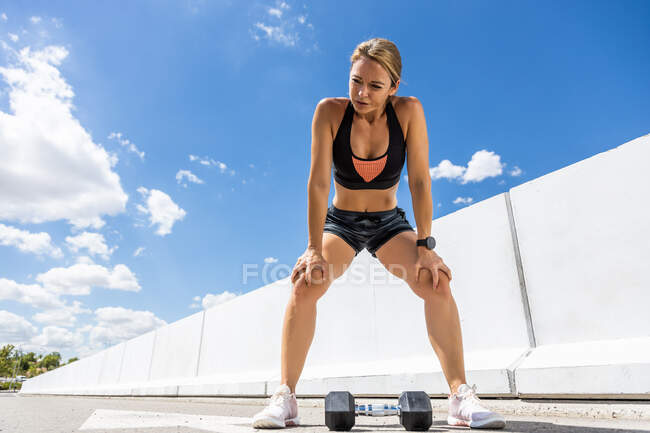 Молодая женщина тренируется с гантели на открытом воздухе, жест усталости, вид спереди — стоковое фото