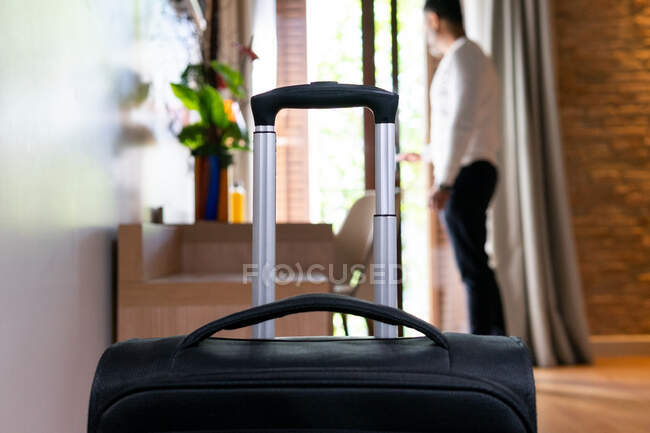 Vista laterale a corpo intero dell'uomo adulto anonimo con apertura bagagli porta balcone in camera d'albergo — Foto stock