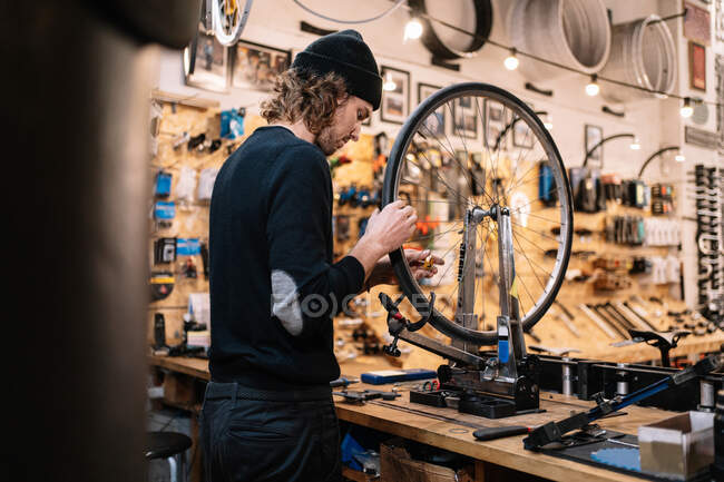 Side view of young male master examining tire on bike wheel while working in professional repair service workshop — Stock Photo