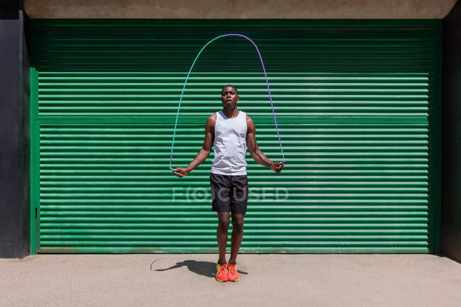 Сфокусований афроамериканець стрибає мотузкою під час тренування на кардіо в сонячний день у місті. — стокове фото
