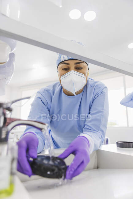 Desde abajo el dentista del cultivo lava chapas con agua limpia en fregadero en clínica dental - foto de stock