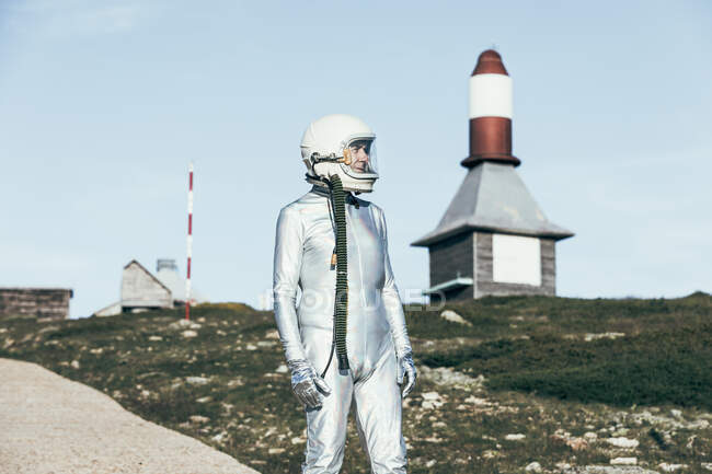 Uomo in tuta spaziale in piedi su un terreno roccioso contro le antenne a forma di razzo a strisce nella giornata di sole — Foto stock