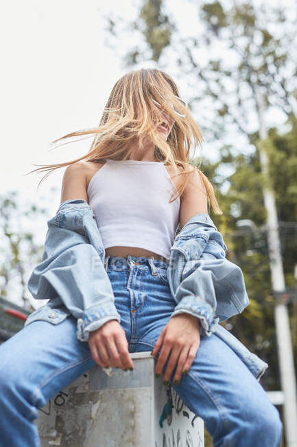 Niedriger Winkel junger entzückter Frauen im Jeans-Outfit, die auf der Straße sitzen und das Wochenende genießen — Stockfoto