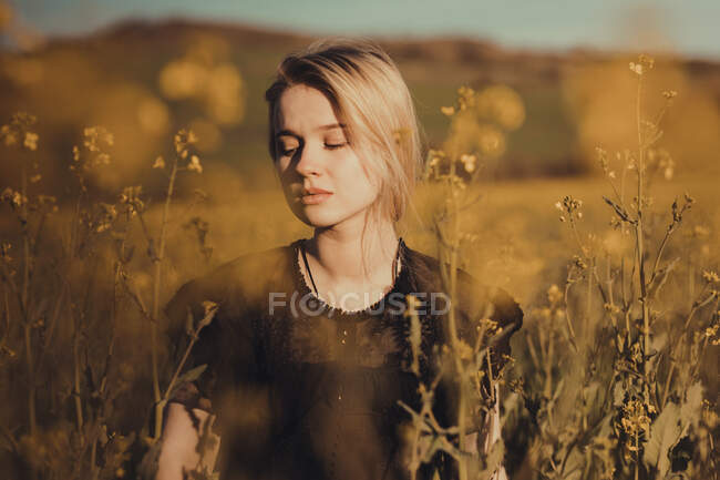 Retrato de una hermosa joven con en el campo con los ojos cerrados entre las flores - foto de stock