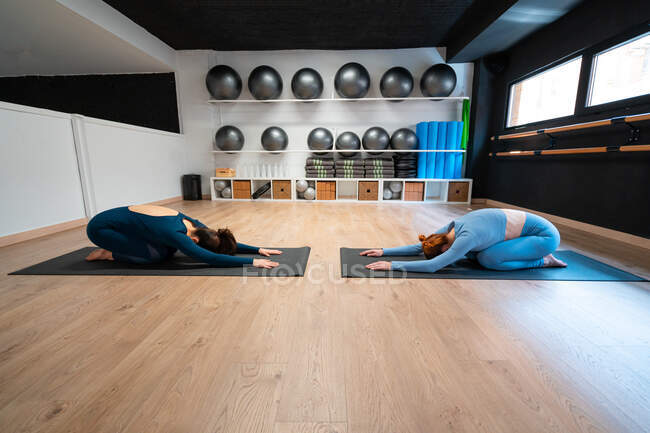 Vue latérale complète du corps des femmes minces et calmes qui posent pendant l'étirement du corps et se relaxent pendant les cours de yoga ensemble dans un studio de fitness — Photo de stock