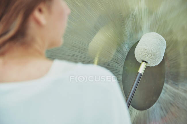 Rückansicht einer erwachsenen Frau in weißer Kleidung mit Schläger, die während der spirituellen Praxis einen schwebenden Gong spielt — Stockfoto