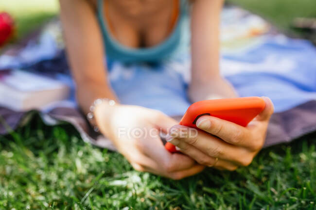 Nahaufnahme einer anonymen Person, die ihr Telefon benutzt, während sie an einem Sommertag im Gras liegt — Stockfoto
