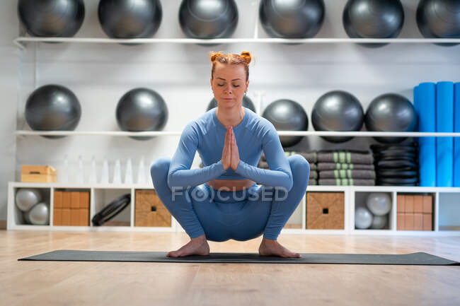 Full body of calm young female doing Garland pose with namaste hands and closed eyes while practicing mindfulness during yoga session in fitness studio — Stock Photo