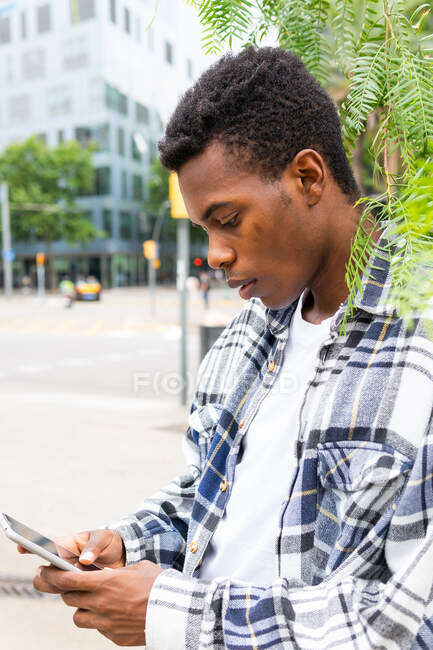 Side view of confident African American male messaging on mobile phone while standing in city street — Stock Photo