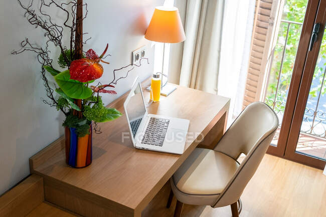 Dall'alto di tavolo con netbook messo vicino a mazzo di piante e bottiglia di succo in appartamento elegante — Foto stock