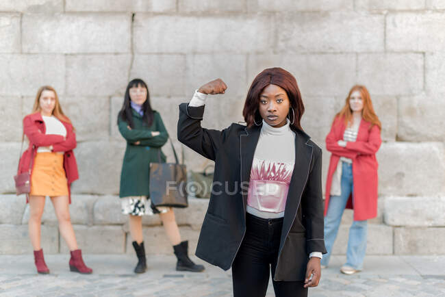 Selbstbewusste Afroamerikanerin zeigt Bizeps, während sie gegen eine Gruppe von multirassischen Frauen steht, die ein Konzept von Girl Power zeigen — Stockfoto