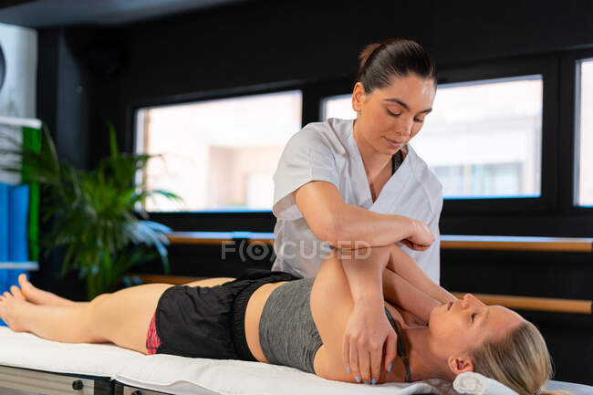 Terapeuta femenina en bata blanca masajeando a la mujer durante la sesión de osteopatía en la clínica - foto de stock