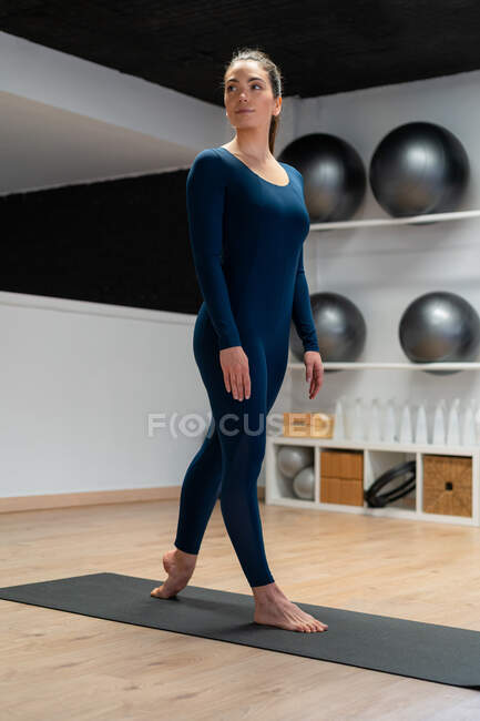 Corps complet de jeune femme en forme en vêtements de sport faisant debout cheville étirer la pose tout en pratiquant le yoga dans le studio de remise en forme regardant loin — Photo de stock