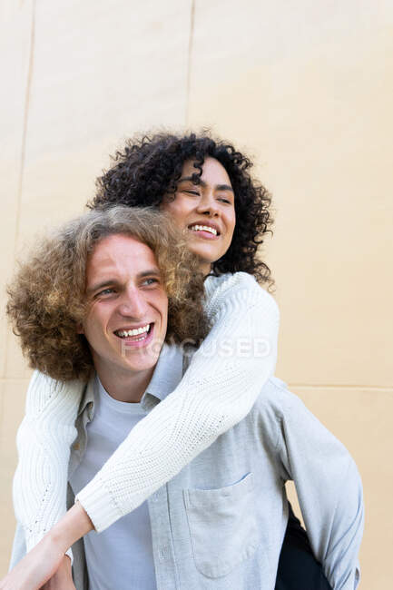 Fröhlicher Mann gibt seiner Freundin Huckepack-Fahrt, beide mit lockigem Haar und lautem Lachen — Stockfoto