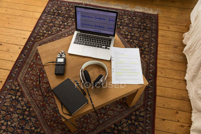 Зверху аудіореєстратор і навушники, розміщені на дерев'яному столі з ноутбуком і блокнотом для запису подкасту вдома — стокове фото