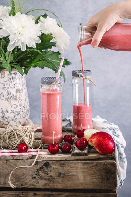 Анонімний врожай наповнює свіжий молочний коктейль нектаринами і вишнею в склянці, розміщеному на дерев'яному столі з фруктами і ягодами — стокове фото
