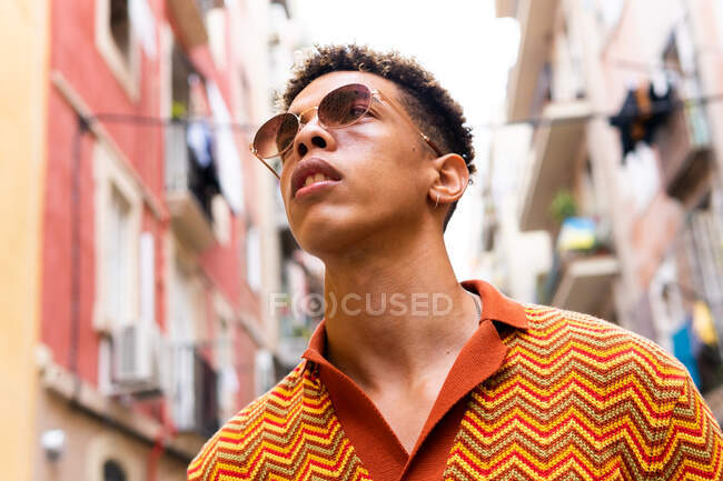 Baixo ângulo de confiante jovem turista étnico masculino olhando para longe enquanto explora antigas ruas estreitas da cidade de Barcelona — Fotografia de Stock