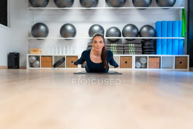 Corps complet de jeune femme faisant pose de sauterelle tout en pratiquant le yoga en studio en regardant la caméra — Photo de stock
