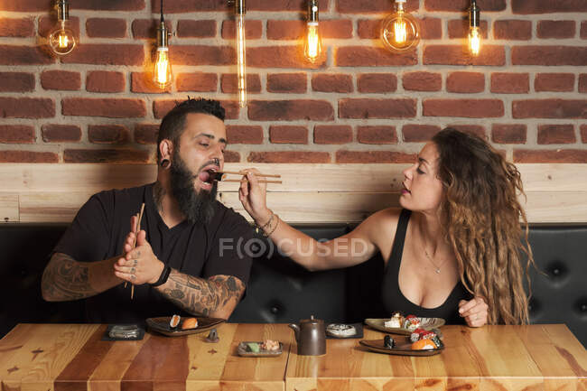 Loving couple eating appetizing sushi while sitting at wooden table in Japanese restaurant — Stock Photo