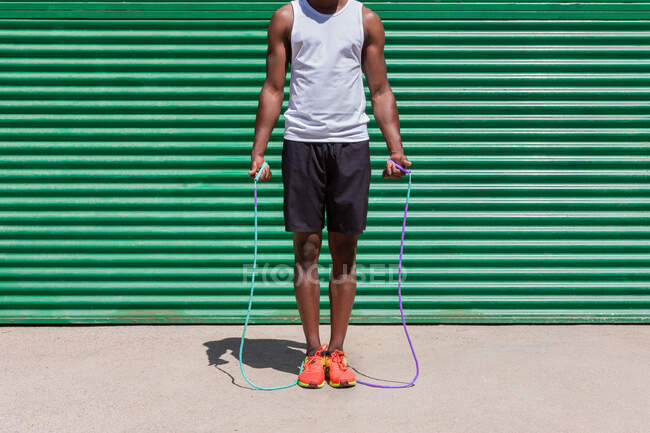 Сфокусований афроамериканець стрибає мотузкою під час тренування на кардіо в сонячний день у місті. — стокове фото