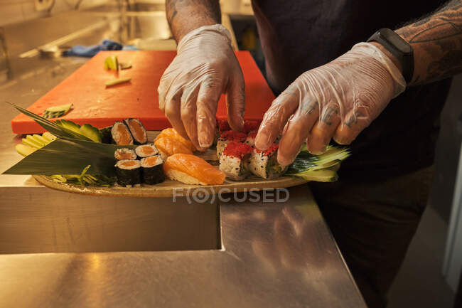 Crop cocinero masculino anónimo que sirve sushi en el plato en la cocina en el restaurante japonés - foto de stock