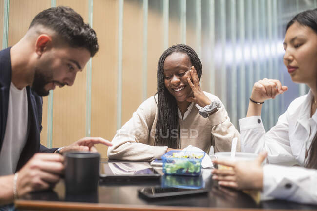 Company of diverse coworkers gathering at table in kitchen and having break while eating lunch — Stock Photo