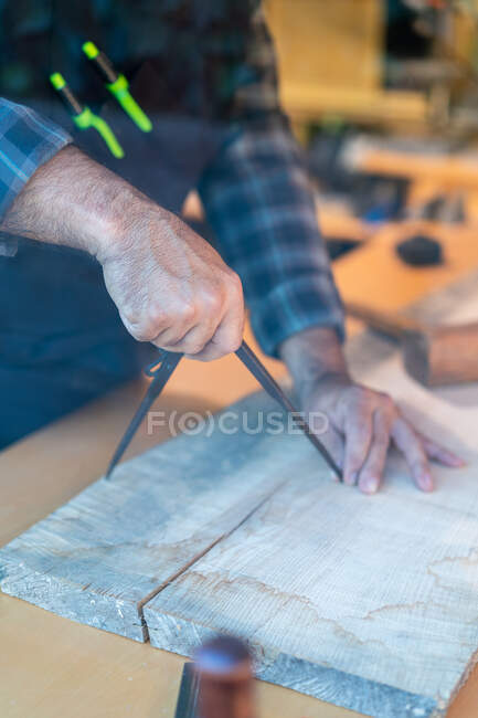 Lavoratore maschio di legno irriconoscibile che utilizza bussola o divisore professionale mentre segna la tavola di legno al banco da lavoro in falegnameria — Foto stock