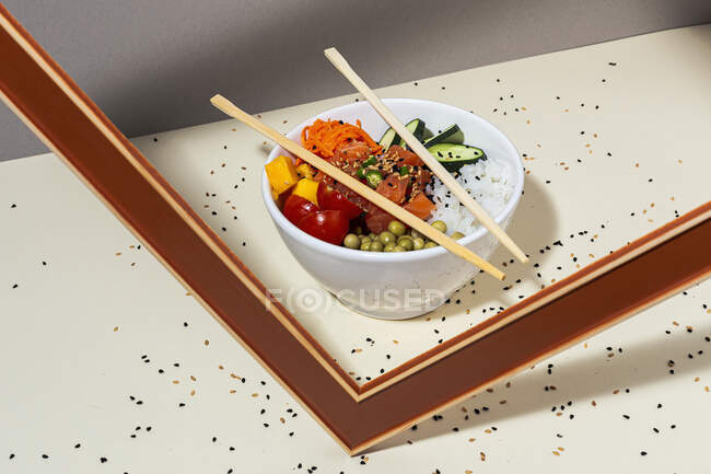 Tigela branca com saboroso prato picante e pauzinhos colocados atrás do quadro na mesa coberta com sementes de gergelim — Fotografia de Stock