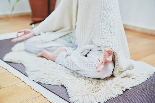 Ritaglio anonimo femminile seduta con gambe incrociate su tappeto soffice durante la pratica dello yoga in camera — Foto stock