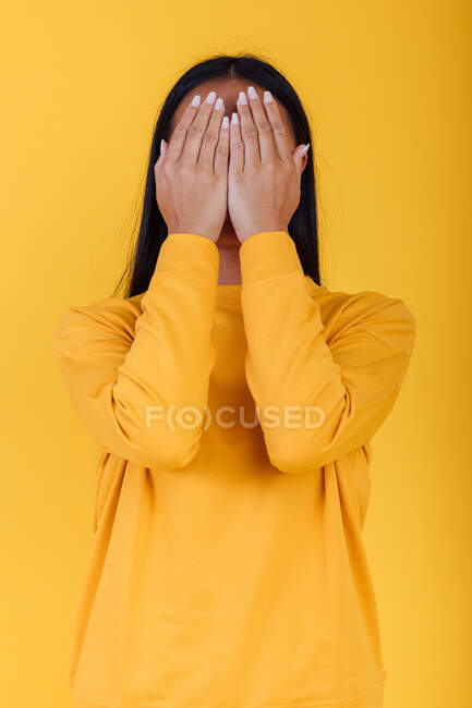 Unrecognizable female covering face with hands on bright yellow background in modern studio — Stock Photo