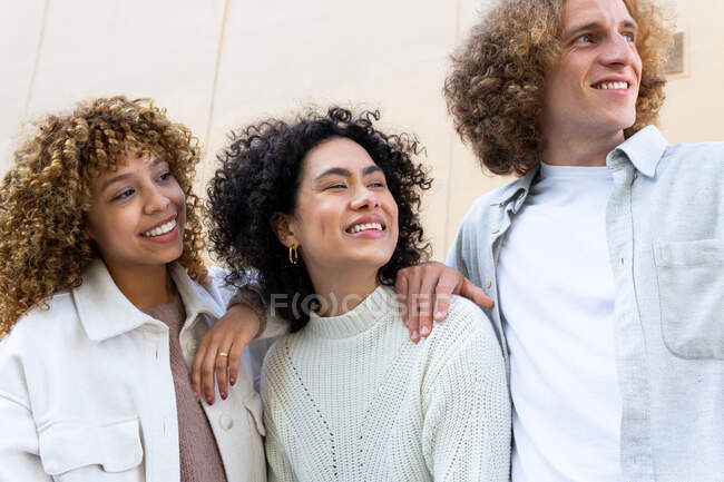 Різноманітний чоловік і жінки з кучерявим волоссям, що стоять, дивлячись від сміху на бежевому фоні — стокове фото