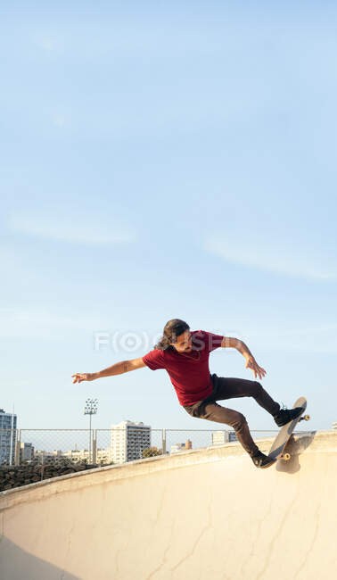 Мужчина скейтбордист, катающийся на скейтборде на платформе под облачным голубым небом в городском скейт-парке в солнечный день — стоковое фото