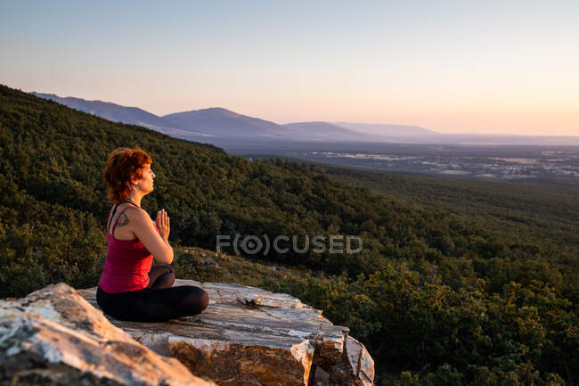 Joven yogi practicando yoga sobre una roca en la montaña con la luz del amanecer - foto de stock