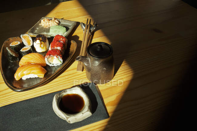 Сверху тарелки с разнообразными суши-роллами подаются на столе с палочками для еды и соевым соусом в японском ресторане — стоковое фото