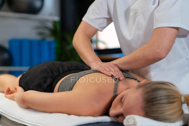 Ritagliato massaggiatrice irriconoscibile sorridente e massaggiare le spalle della donna mentre si lavora in clinica fisioterapia — Foto stock
